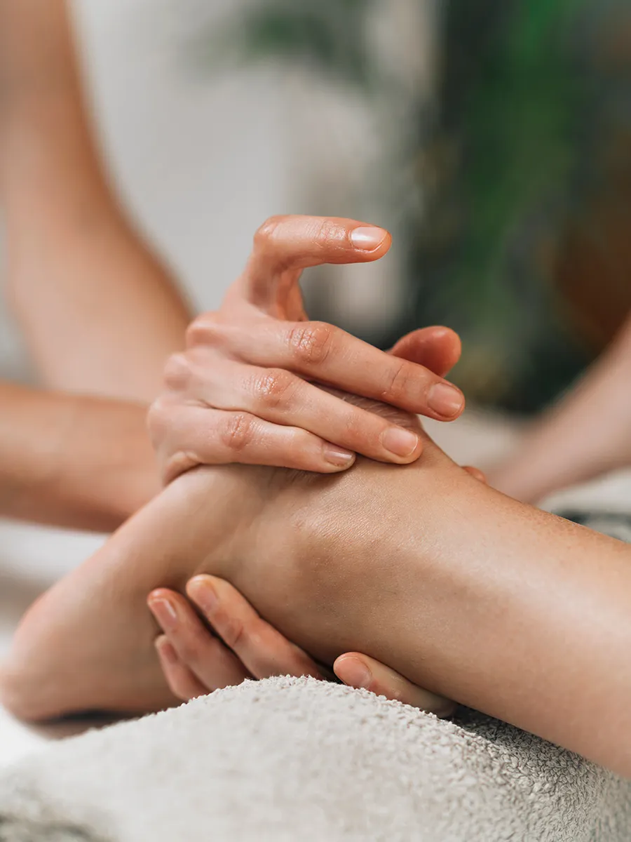 Reflexologist gently massaging pressure points on the top and side of a client's foot during a therapy session