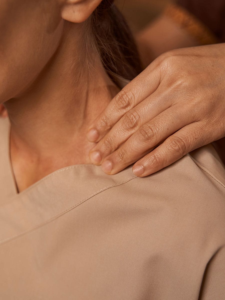 Close-up of a practitioner's hand gently touching and assessing a patient's shoulder and neck area during a physical therapy session.