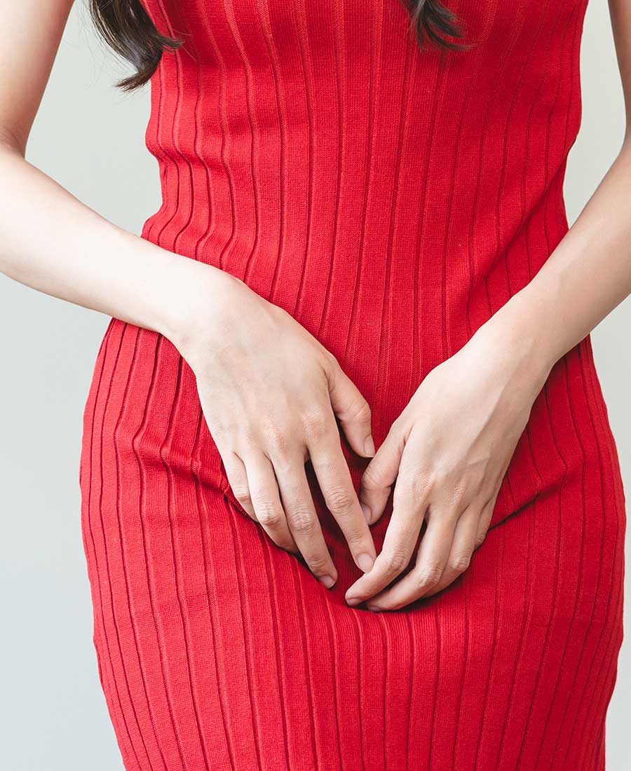 Close-up of a woman in a red ribbed dress holding her hands over her lower abdomen, suggesting menstrual pain or cramps.