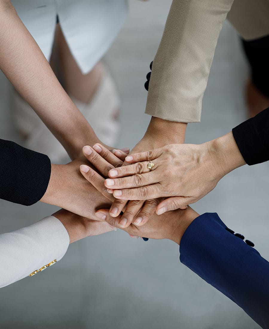 An overhead photograph captures six diverse people in professional attire stacking their hands together, symbolizing unity and teamwork.