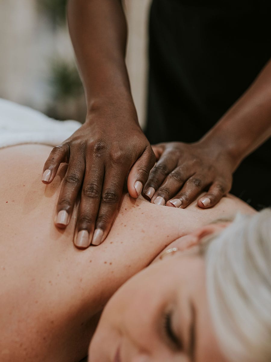 A close-up of a massage therapist's hands applying pressure to a woman's upper back and shoulders.